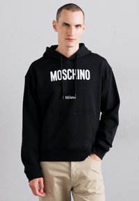 Sweatshirt negru cu glugă, fabricat din bumbac, având un logo alb îndrăzneț "MOSCHINO" și un buzunar frontal tip kangaroo.