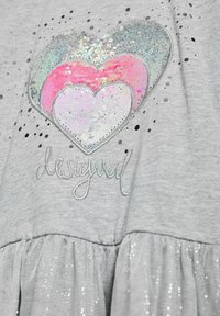 Sivi odjevni predmet s blistavim dizajnom srca koje sadrži šljokice u srebrnoj, ružičastoj i iridescentnim bojama. Uključuje izvezeno "desigual" u srebrnoj boji.