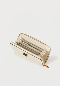 Crème portemonnee met ritssluiting, gouden hardware en zwarte accenten. Interieur beschikt over meerdere vakken en een ritssluitingscompartiment.