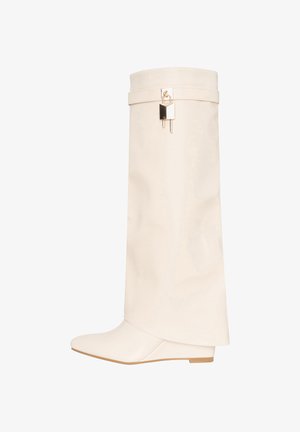 Hoge laarzen van crèmekleurig leer met een puntige neus, lage sleehak en een gouden hangslotdetail bij de bovenrand.