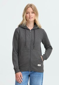 Felpa grigia con zip, cappuccio regolabile con cordino, tasche frontali, polsini e orlo a coste. Tessuto leggermente strutturato, etichetta a marchio in basso.