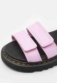 Sandálias de pele sintética roxa com duas tiras ajustáveis em Velcro, palmilha texturizada preta e sola de borracha preta com costura amarela.
