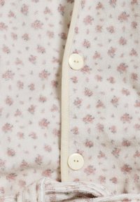 Blommönstrad tyg i mjuk krämfärg med små rosa och grå blommor. Har en beige knapp och dragsko i midjan.