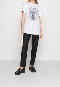 Bílá bavlněná trička s tištěným architektonickým designem. V kombinaci s černými upravenými kalhotami a robustními černými botami se sponou.