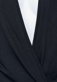 Svart, lätt jersey tyg har en djup V-ringning med överlappande delar som framhäver den släta texturen och den figurnära passformen.