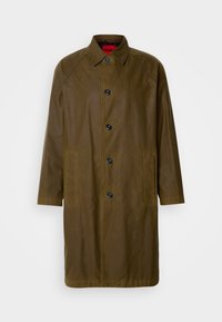 Long manteau homme vert olive avec col pointu, cinq boutons noirs et deux poches latérales, présenté sur un fond blanc uni.