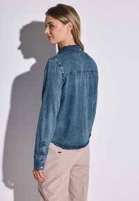 Camisa de mezclilla de botones en azul oscuro con cuello, mangas largas y puños de botón; presenta un diseño limpio en la parte posterior y una textura de tela suave.