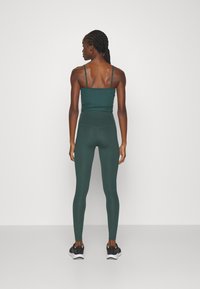 Soutien-gorge de sport vert foncé avec de fines bretelles, associé à un legging taille haute assorti, mettant en valeur une texture lisse et une coupe ajustée.