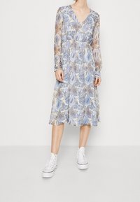 Kevyt, pitkähihainen mekko V-purkauksella, jossa on sinivalkoinen paisley-kuvio. Yhdistetty valkoisiin tennareihin.