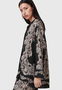 Blusa nera a maniche lunghe caratterizzata da un intricato motivo paisley beige, vestibilità ampia e una trama di tessuto liscia. Bottoni lungo la parte anteriore.