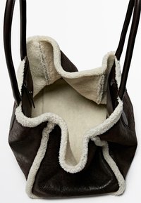 Bruine leren handtas met een zachte crèmekleurige voering. Voorzien van twee stevige handvatten en een gegolfd, open ontwerp voor gemakkelijke toegang.