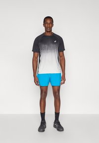 Ανδρικά αθλητικά ρούχα με μπλουζάκι σύντομων μανικιών που παρουσιάζει σταδιακή μετάβαση από μαύρο σε λευκό και έντονα μπλε σορτς, κατασκευασμένα από υλικά που αναπνέουν.