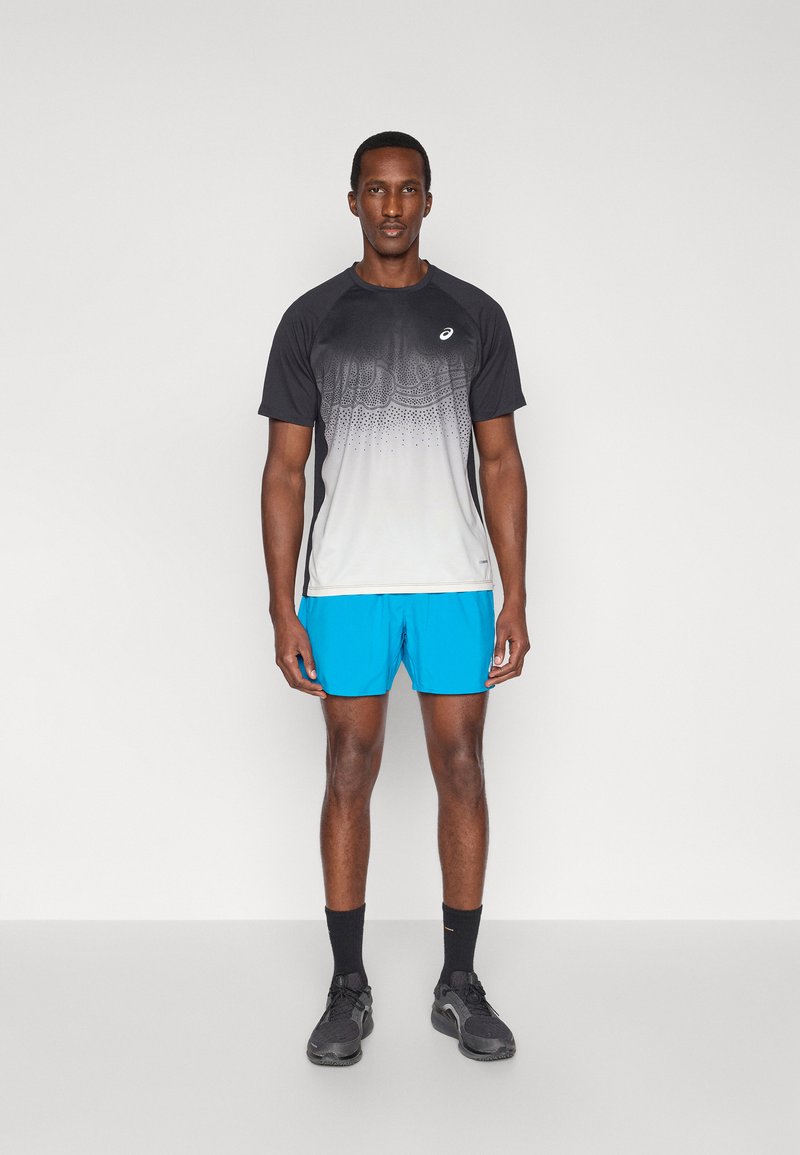 Vêtements de sport pour hommes comprenant un t-shirt à manches courtes à dégradé noir-blanc et un short bleu vif, fabriqués avec des matériaux respirants.
