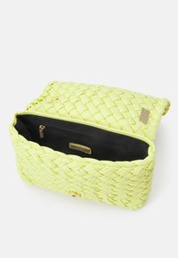 Borsa a tracolla intrecciata di colore giallo neon con finitura testurizzata, dotata di chiusura in metallo dorato e un interno a contrasto di colore nero con tasca con zip.