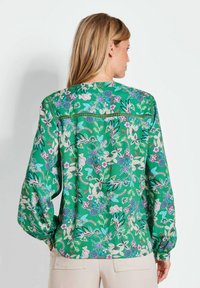Groene bloemetjesblouse met lange mouwen, met een levendig patroon van bloemen en bladeren. Zachte stof en gehaalde details op de schouders.