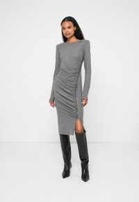 Vestido cinza de mangas compridas com detalhe franzido na lateral e uma fenda com zip. Combinado com botas pretas até ao joelho, apresentando um design de biqueira apontada.