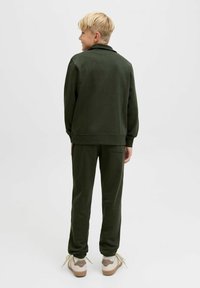 Grön sweatshirt och matchande joggers i mjukt tyg. Sweatshirten har en avslappnad passform; joggers har elastiska muddar. Avslappnade skor i kräm och beige.