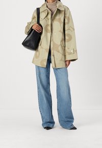 Chaqueta oversize color caqui con patrón de flores, combinada con jeans de pierna ancha de color azul claro y bolso negro, con zapatos negros de punta.