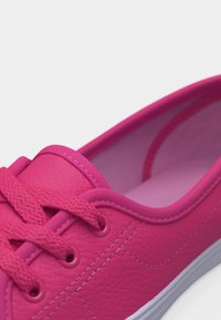 Κοντινό πλάνο ενός φωτεινού ροζ αθλητικού παπουτσιού με υφασμάτινα κορδόνια και λεπτομερή ραφή σε λευκό φόντο.