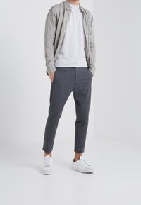 Jasnoszara lniana koszula na guziki noszona na białej podkoszulce z okrągłym dekoltem, zestawiona z szarymi dopasowanymi spodniami i białymi trampkami. Czysty i nowoczesny design.