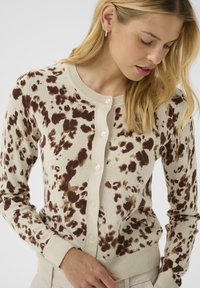 Knit cardigan featuring a cream base with brown spotted pattern, crew neckline, buttons down the front, and ribbed cuffs and hem.