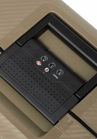 Lucchetto nero approvato dalla TSA con tre quadranti per la combinazione e un foro per la chiave su una superficie di bagaglio beige e testurizzata.