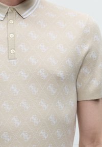 Polo beige à manches courtes avec motif léopard blanc, col à boutons et poignets côtelés porté par une personne.