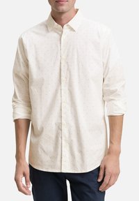 Helle kremfarbene Button-Up-Hemd mit kleinem braunen Punktmuster, langärmelige, hochgerollte Ärmel, aus Baumwollmaterial, spitzen Kragen und vorderer Knopfleiste.