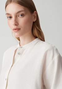 Camicia bianca leggera con colletto alla cinese, maniche corte e chiusura con bottoni. Texture liscia con una vestibilità comoda.