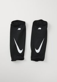 Protège-tibias Nike noirs avec logos Swoosh blancs et petite inscription "MD" blanche, posés à plat sur un fond blanc.