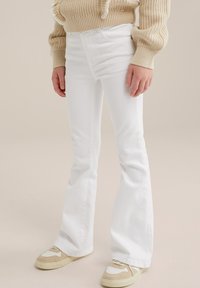 Vita utsvängda jeans av denim, med framfickor, subtil sömnad och en mjuk yta, tillsammans med beige sneakers.