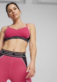 Sujetador deportivo rosa con correas ajustables y una banda negra con logo. Leggings rosa de tiro alto con paneles laterales negros y detalles blancos.