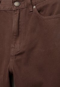 Pantaloni din bumbac maro cu închidere prin buton, bucăți pentru curea și buzunare frontale. Textură netedă cu un luciu ușor, design structurat.
