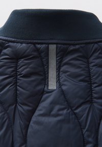 Colletto in tessuto trapuntato blu navy, con texture a coste, caratterizzato da un'etichetta verticale grigia e dettagli di cucitura visibili sul tessuto.