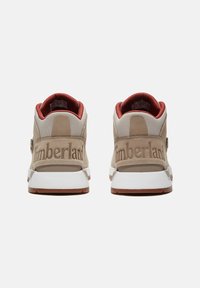Beige Sneakers mit einem Obermaterial aus Wildleder und Mesh. Weiße Gummisohle, rotes Innenfutter und geprägtes "Timberland"-Logo auf der Rückseite.
