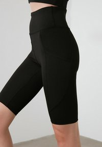 Shorts da bicicletta neri a vita alta realizzati in tessuto elasticizzato con una texture liscia, dotati di tasche laterali e di una silhouette aderente.