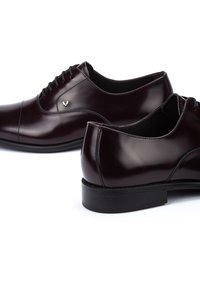 Chaussures habillées en cuir bordeaux avec une finition lisse, un design à lacets, des coutures subtiles et un petit accent logo en argent sur le côté.