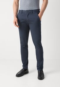 Chinos blu navy realizzati in tessuto misto cotone, caratterizzati da una vestibilità slim, tasche frontali e una texture liscia, abbinati a mocassini neri.