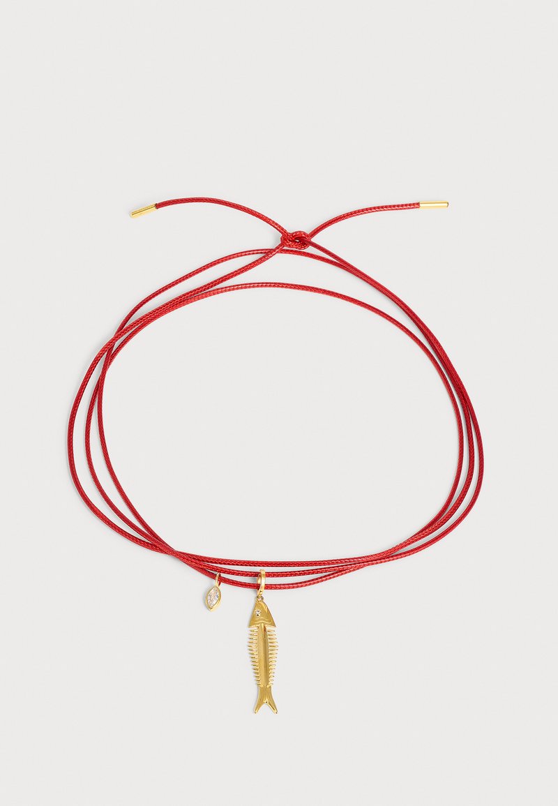 Bracelet réglable en cordon rouge avec un pendentif arête de poisson doré et un petit pendentif doré en forme de marquise avec une pierre claire sur fond clair.