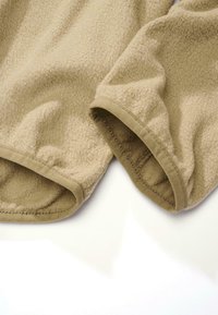 Beige bolyhos anyag, puha tapintással, lekerekített ujjnyílásokkal és sima, kontrasztos bézs szegéllyel.