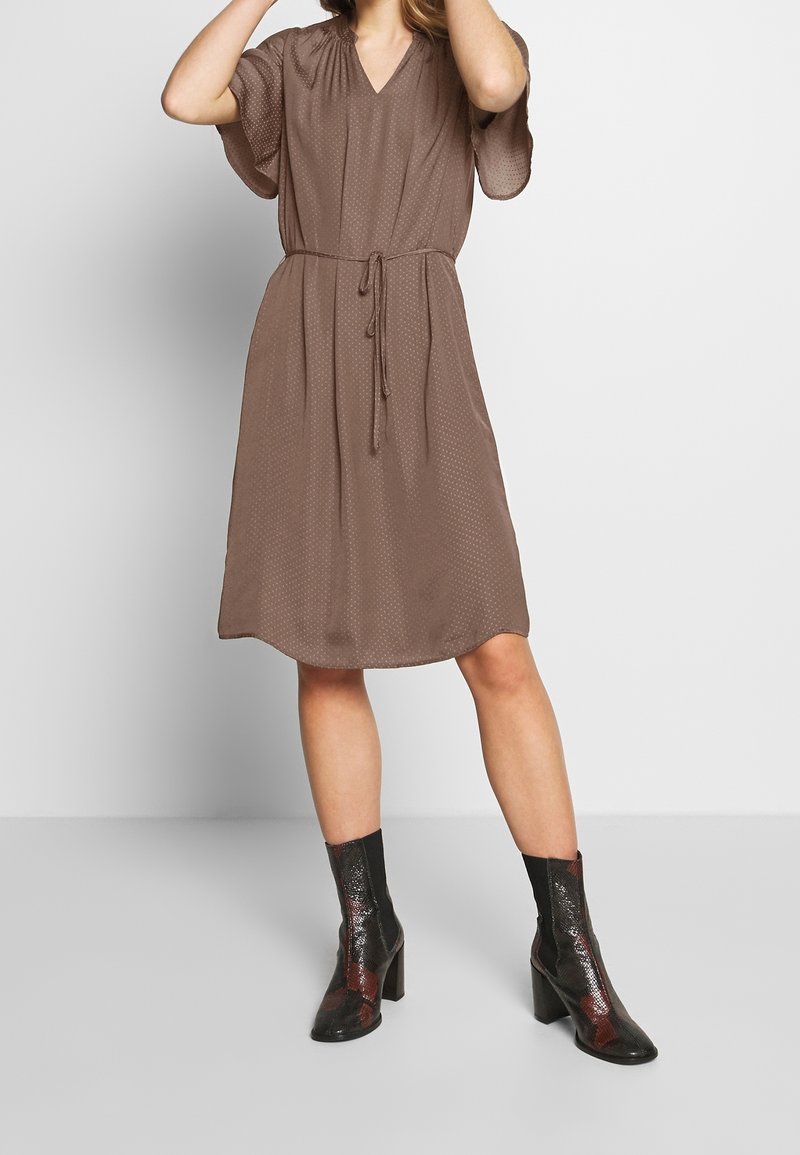 Brown polka dot dress with short sleeves, V-neck, and a tie waist. Worn with shiny black and red ankle boots featuring a block heel.