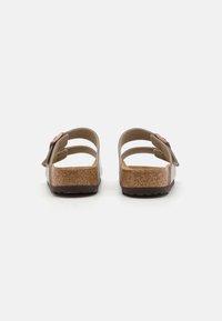 Sandal cu talpă din plută de culoare maro, cu două curele superioare ajustabile, un accent decorativ sub formă de floare și o talpă din cauciuc texturat.