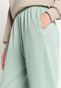 Calças jogger leves de algodão verde menta, com cintura elástica e bolsos laterais, apresentando um corte relaxado e uma textura suave.