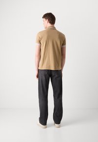 Khaki Poloshirt mit weißem gestreiften Kragen, kombiniert mit dunklen Jeans und weißen Sneakers. Das Shirt ist tailliert und hat eine glatte Textur.