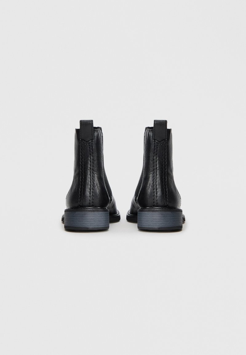 Schwarze Leder-Ankle Boots mit glatter Oberfläche, elastischen Seiteneinsätzen und niedrigem, gestapeltem Absatz. Mit einer Ziehschlaufe für einfaches Anziehen.