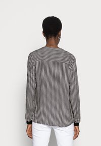 Chemise à manches longues avec un motif noir et blanc et des accents rouges subtils. Présente un col arrondi et des poignets noirs. Texture de tissu lisse.