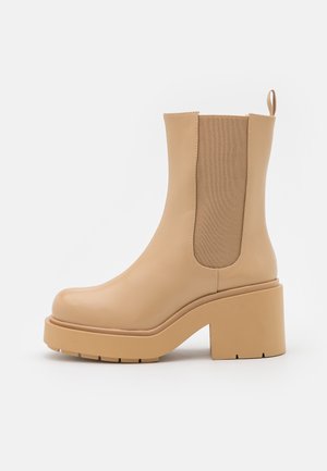 Bottine beige à talon bloc épais, avec panneau latéral élastique pour un ajustement facile et languette de tirage, sur fond blanc.