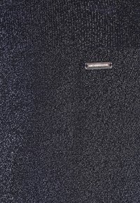 Dunkelblauer Pullover mit schimmernder Textur, ausgestattet mit einem kleinen silbernen Markenetikett nahe dem Ausschnitt und gerippten Bündchen.
