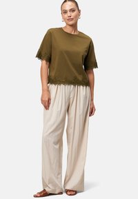 Olive green short-sleeve top with lace trim at hem, paired with cream wide-leg trousers and brown sandals. Smooth fabric texture.