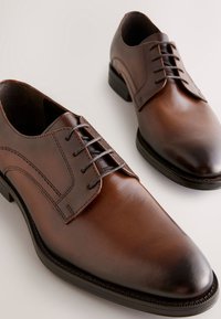 Brune lædersko med glat tekstur, lukket snøresystem og subtile syningsdetaljer. Rundet tå og lav hældesign.